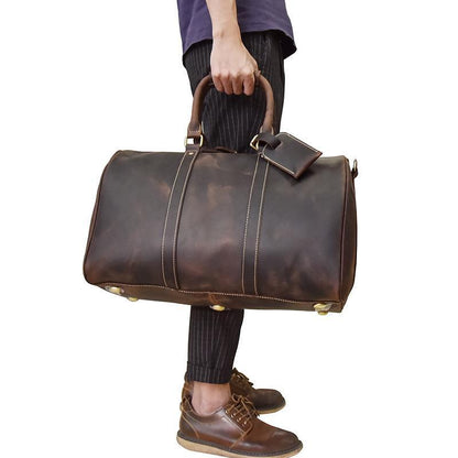 Person holding a brown leather duffel bag on a white background