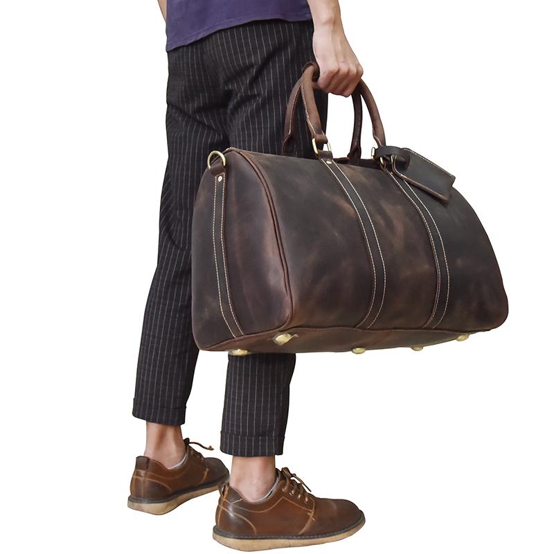 Person holding a brown leather duffel bag with striped pants and brown shoes on a white background