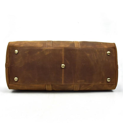 Brown leather bag with gold studs on bottom of duffle, shown on a white background