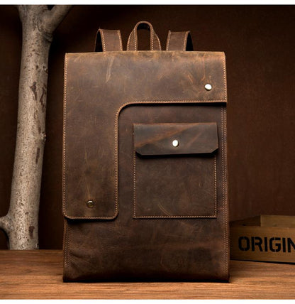 Brown leather backpack with a front pocket on a wooden surface.