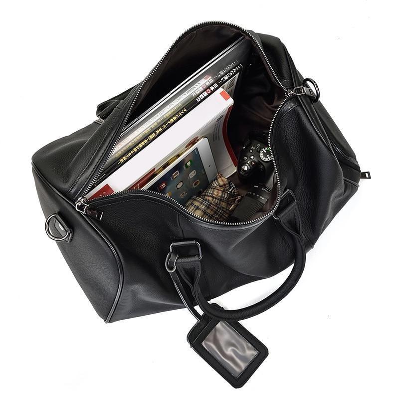 Black leather duffel bag with compartments containing a smartphone, tablet, and other items on a white background