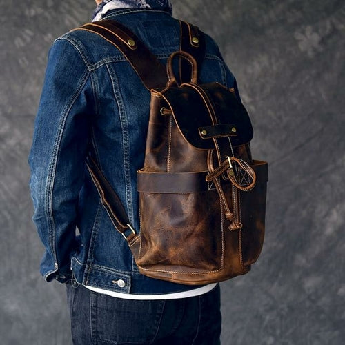 Person wearing a brown leather backpack with a denim jacket on a gray background