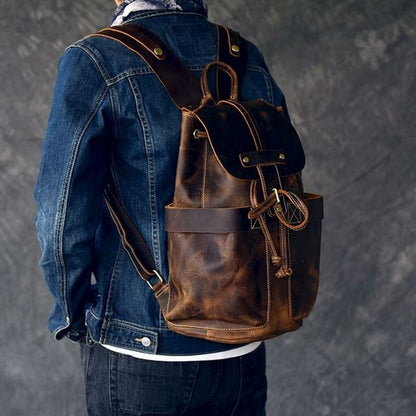 Person wearing a brown leather backpack with a denim jacket on a gray background
